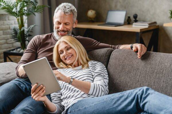 Happy senior couple using digital tablet on sofa indoors